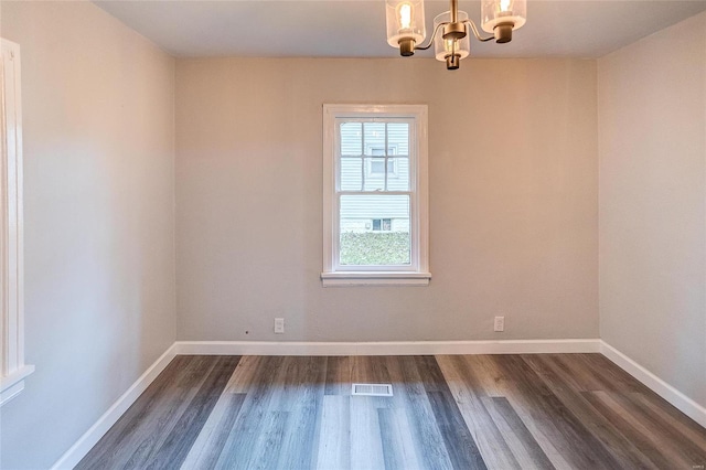 spare room featuring a chandelier, dark wood-style floors, and baseboards