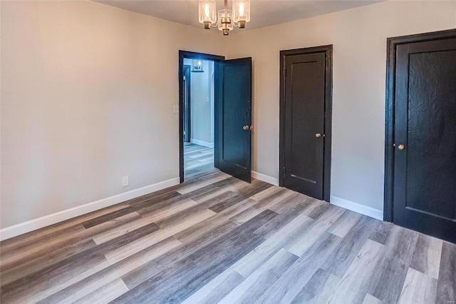 unfurnished bedroom featuring a chandelier, wood finished floors, and baseboards