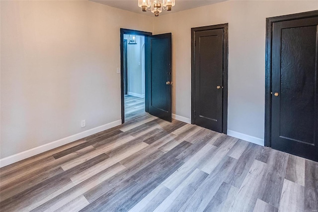 unfurnished bedroom featuring a chandelier, wood finished floors, and baseboards