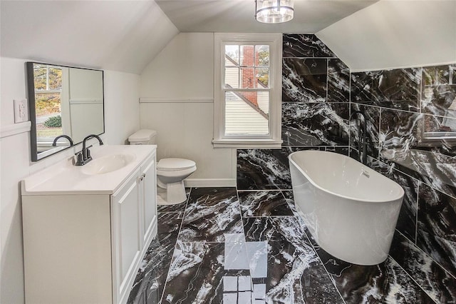 full bathroom featuring marble tiled floors, a freestanding tub, vanity, lofted ceiling, and toilet
