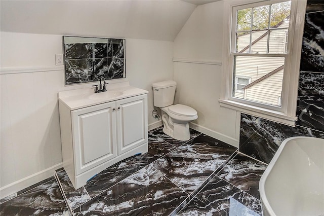 full bathroom with marble tiled floors, a freestanding tub, lofted ceiling, toilet, and baseboards