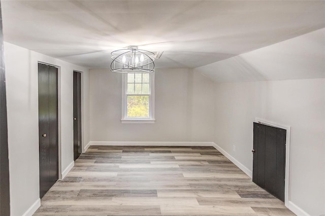 unfurnished dining area with a chandelier, light wood-type flooring, baseboards, and vaulted ceiling