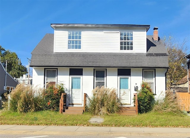 view of front facade with roof with shingles and a chimney
