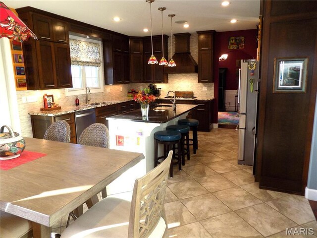 13185 Jenna Ln, Rolla, MO 65401 - kitchen with custom exhaust hood, appliances with stainless steel finishes, a kitchen island with sink, a sink, and backsplash