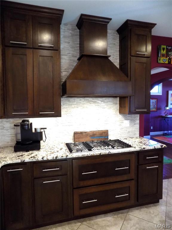 13185 Jenna Ln, Rolla, MO 65401 - kitchen featuring custom exhaust hood, decorative backsplash, light stone countertops, and dark brown cabinetry