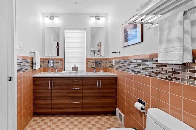 full bathroom featuring tile walls, toilet, double vanity, wainscoting, and tile patterned floors