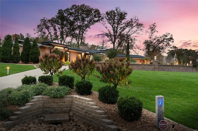 yard at dusk featuring a lawn