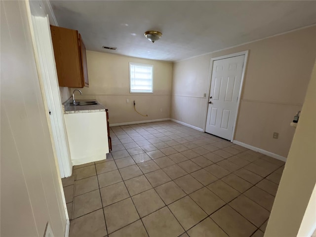 kitchen featuring light tile patterned flooring, light countertops, a sink, baseboards, and brown cabinetry