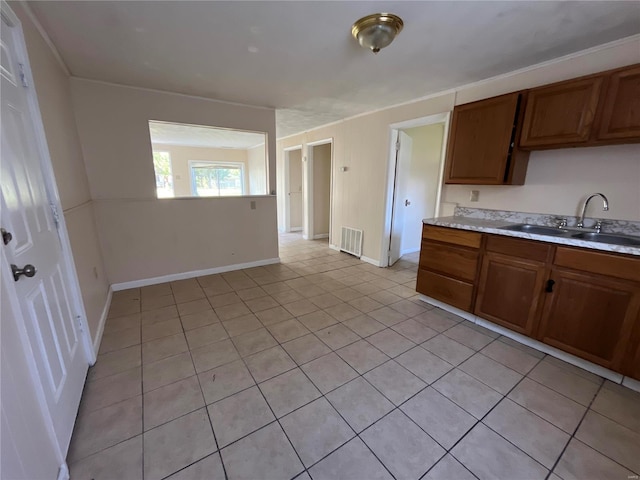 kitchen with a sink, light countertops, light tile patterned floors, baseboards, and brown cabinets