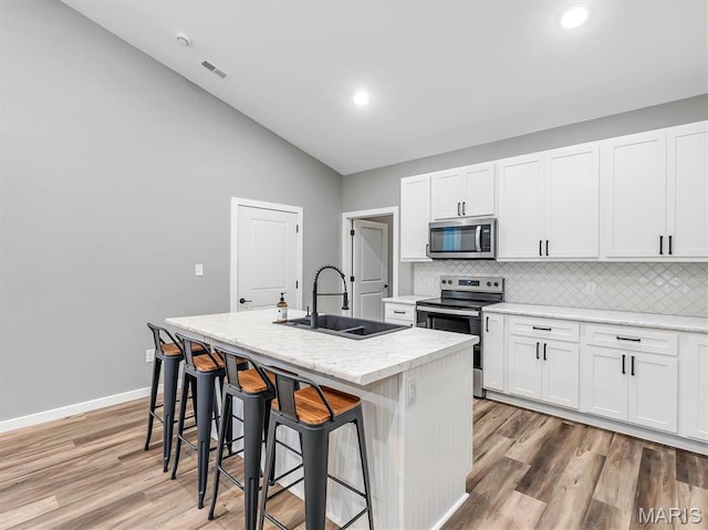 60 Cedar Brook Dr, Pacific, MO 63069 - kitchen featuring appliances with stainless steel finishes, a kitchen island with sink, light wood finished floors, decorative backsplash, and vaulted ceiling