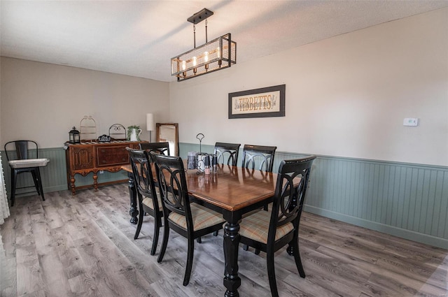 dining space with wood finished floors, a wainscoted wall, and a chandelier