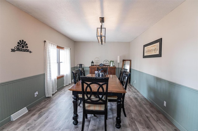 dining space featuring a wainscoted wall, wood finished floors, and a textured ceiling