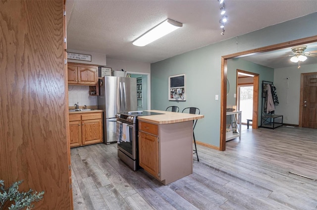 kitchen featuring appliances with stainless steel finishes, light wood finished floors, a sink, a breakfast bar, and tile counters