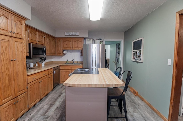 kitchen featuring appliances with stainless steel finishes, light wood-style floors, a textured ceiling, butcher block countertops, and backsplash