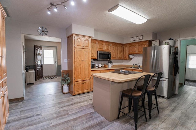 kitchen featuring appliances with stainless steel finishes, light wood-style flooring, a kitchen bar, a center island, and a textured ceiling