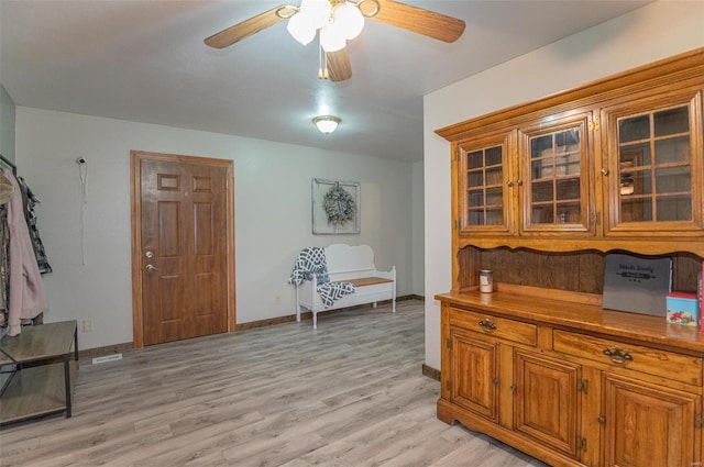 kitchen featuring brown cabinets, a ceiling fan, light wood-style flooring, and glass insert cabinets
