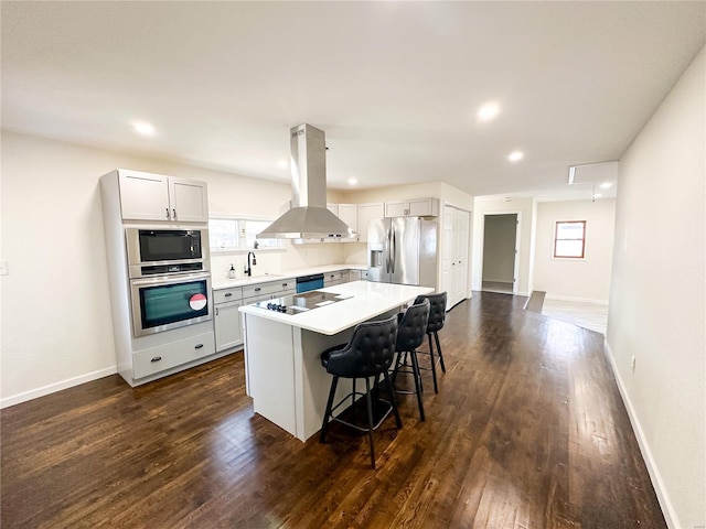 kitchen with stainless steel appliances, island exhaust hood, a kitchen bar, dark wood-style flooring, and light countertops