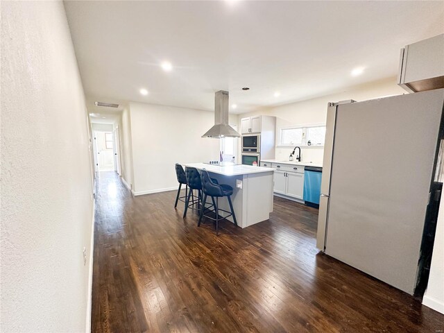 kitchen with appliances with stainless steel finishes, island exhaust hood, a center island, dark wood-style flooring, and a kitchen bar