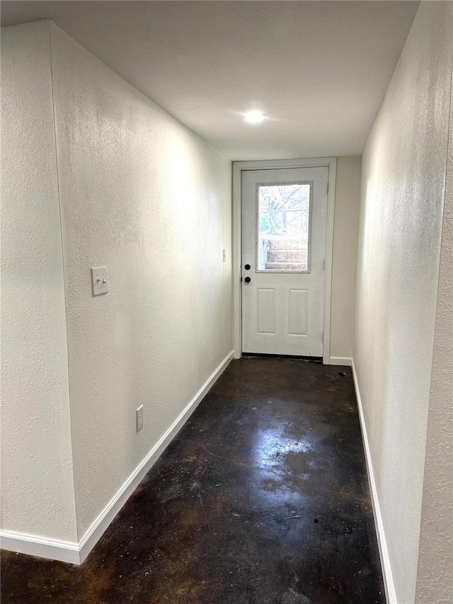 doorway to outside with baseboards, concrete flooring, and a textured wall