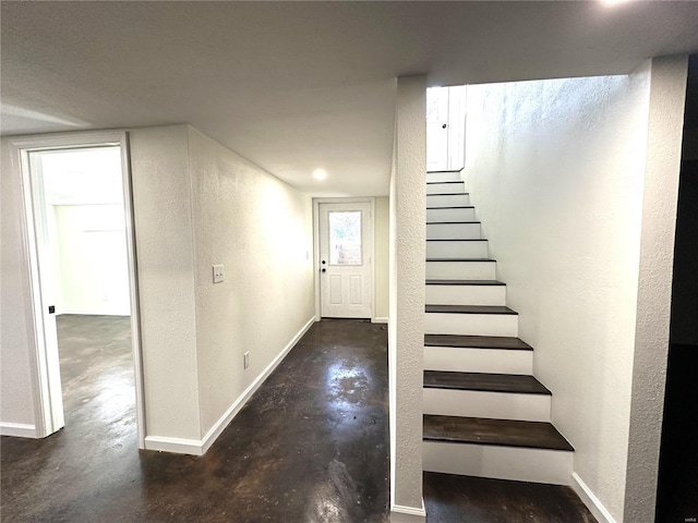 stairs featuring a textured wall, baseboards, and finished concrete flooring