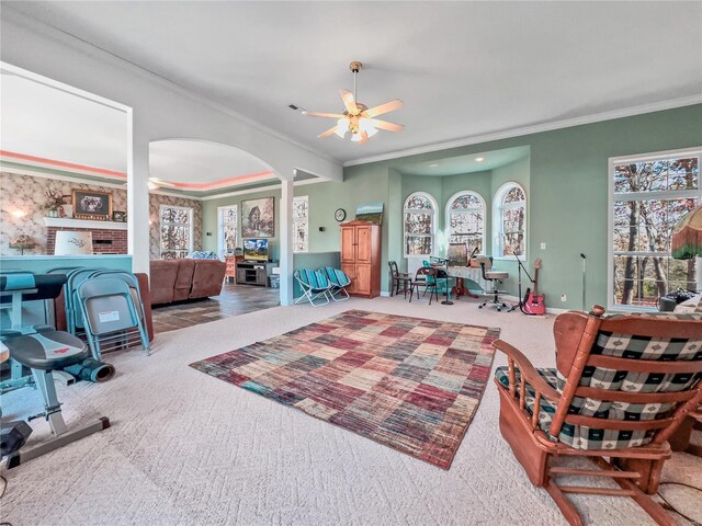 living area with crown molding, a ceiling fan, carpet floors, arched walkways, and plenty of natural light
