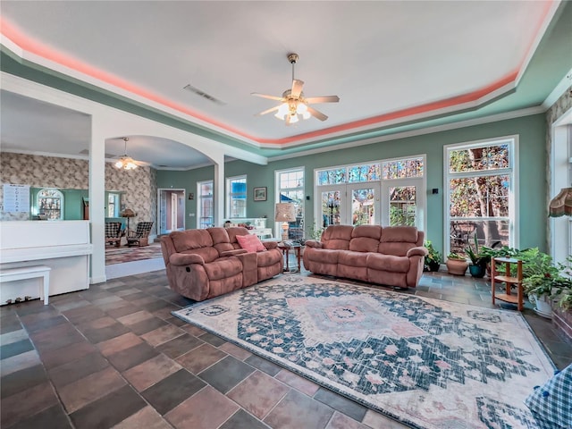 living area with a ceiling fan, a raised ceiling, crown molding, stone finish flooring, and arched walkways