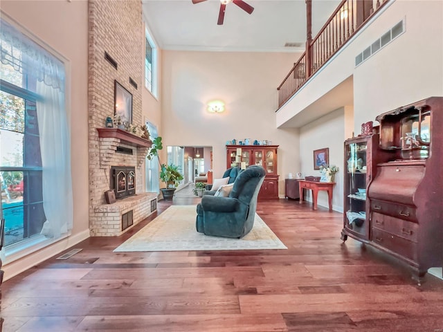 living area featuring a towering ceiling, ceiling fan, a fireplace, wood finished floors, and baseboards