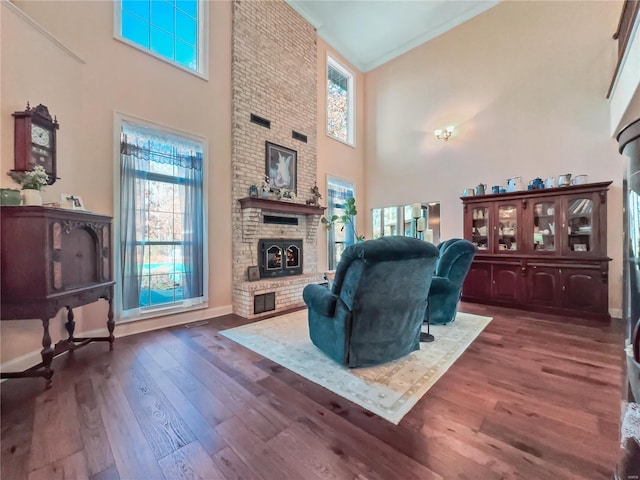 living area with a towering ceiling, a brick fireplace, healthy amount of natural light, dark wood finished floors, and baseboards