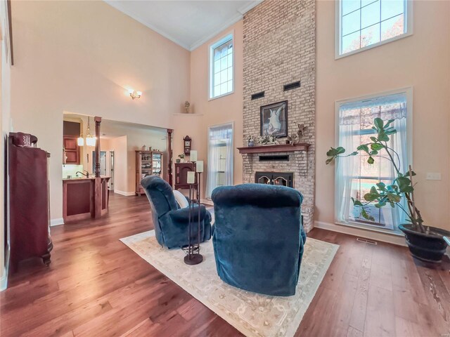 living area with a high ceiling, a fireplace, wood finished floors, baseboards, and crown molding