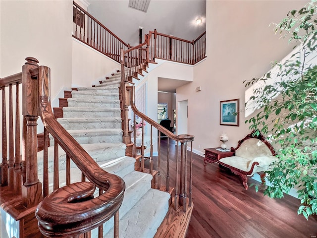 stairway with wood finished floors, baseboards, and a high ceiling