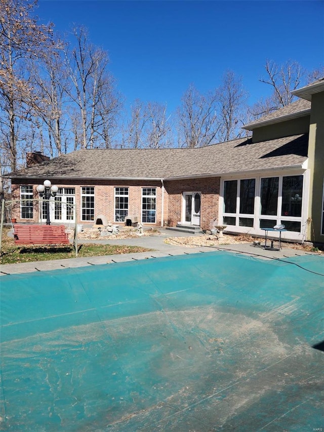 back of property with a covered pool, brick siding, and a shingled roof