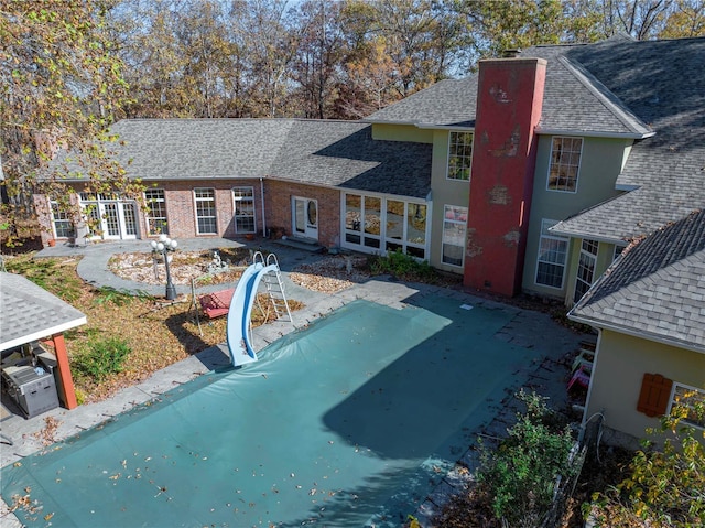 back of property featuring roof with shingles, an outdoor pool, and stucco siding