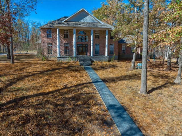 greek revival house featuring brick siding, covered porch, and a front lawn