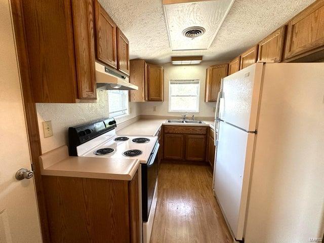 kitchen featuring freestanding refrigerator, under cabinet range hood, electric range oven, a sink, and brown cabinets