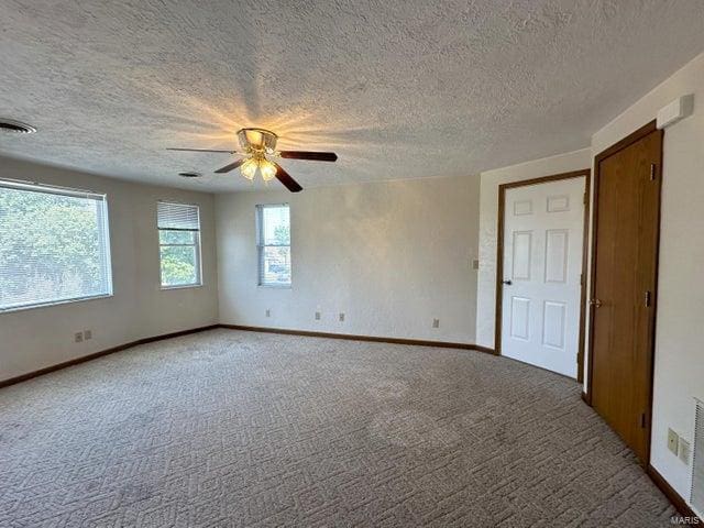 empty room with a ceiling fan, a textured ceiling, light carpet, and baseboards