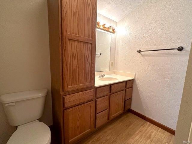 half bath with a textured wall, wood finished floors, vanity, toilet, and a textured ceiling