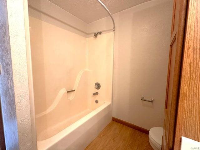 full bath featuring wood finished floors, toilet, tub / shower combination, and baseboards