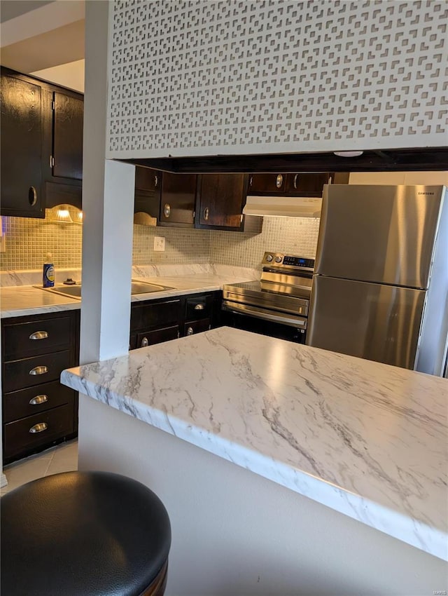 kitchen with appliances with stainless steel finishes, backsplash, under cabinet range hood, and light stone countertops
