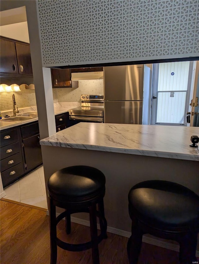 kitchen with appliances with stainless steel finishes, a sink, extractor fan, tasteful backsplash, and a breakfast bar area