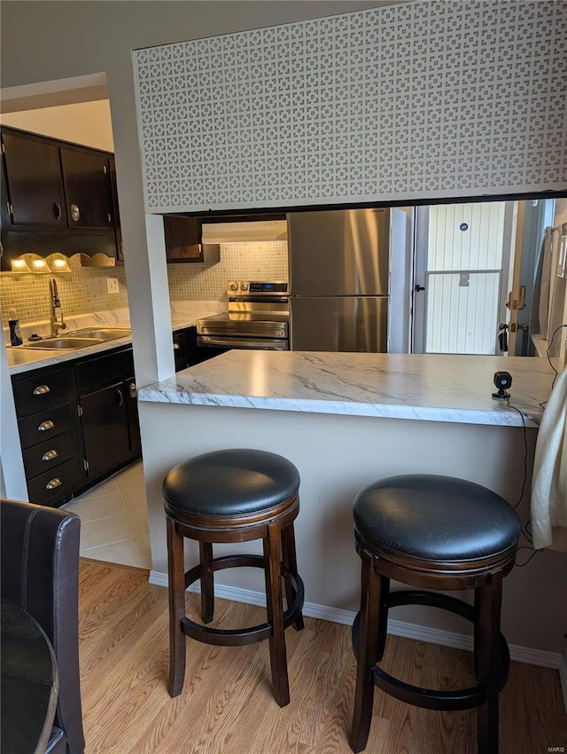 kitchen featuring appliances with stainless steel finishes, a sink, range hood, and a breakfast bar area