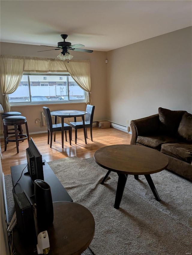 living area with a baseboard heating unit, a ceiling fan, light wood-style flooring, and baseboards