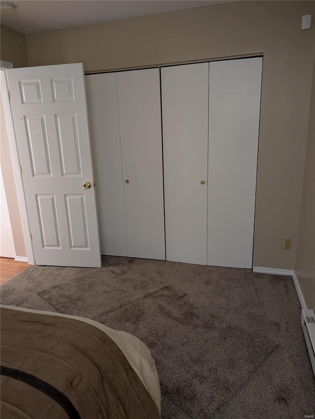 unfurnished bedroom featuring carpet, a closet, and baseboard heating