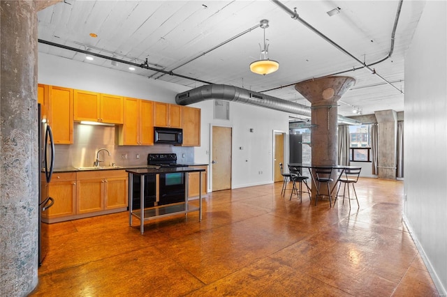 kitchen with black appliances, a sink, baseboards, a towering ceiling, and concrete floors
