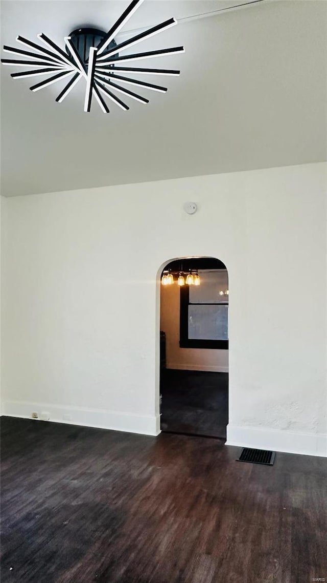 empty room with arched walkways, wood finished floors, baseboards, and a smoke detector