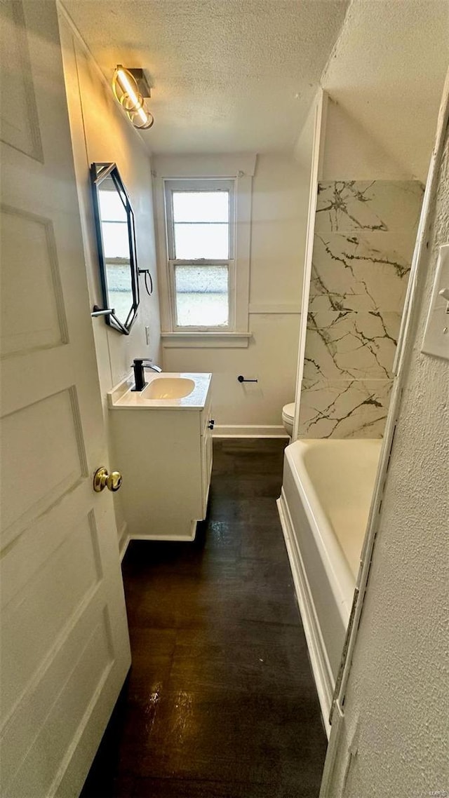 full bathroom featuring a textured ceiling, vanity, wood finished floors, a bath, and toilet