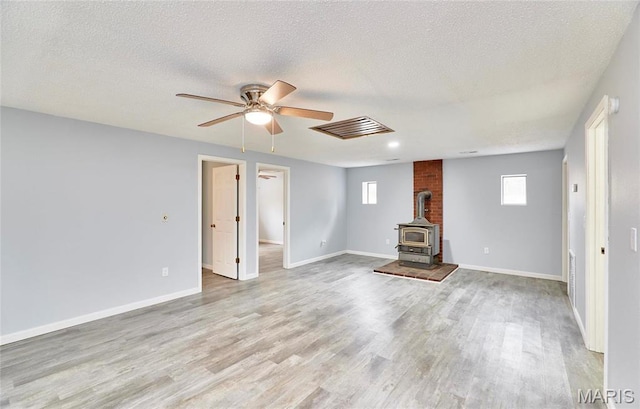 10994 Webster Rd, Caledonia, MO 63631 - unfurnished living room with a wood stove, ceiling fan, light wood finished floors, plenty of natural light, and a textured ceiling