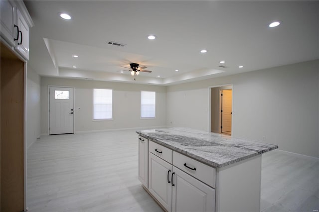 kitchen with a ceiling fan, a tray ceiling, light wood finished floors, a center island, and recessed lighting