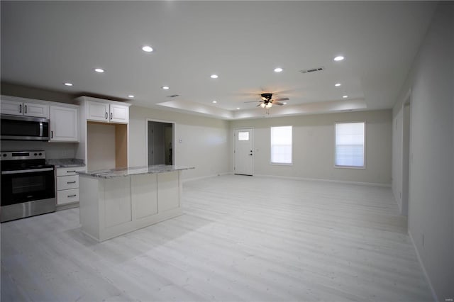 kitchen with appliances with stainless steel finishes, a raised ceiling, light wood-type flooring, open floor plan, and baseboards