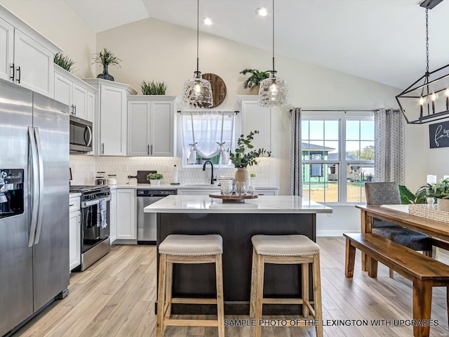kitchen with appliances with stainless steel finishes, a sink, decorative backsplash, a center island, and light wood-style floors