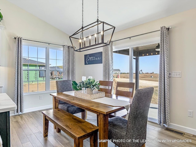 dining area featuring baseboards, light wood finished floors, a chandelier, and vaulted ceiling